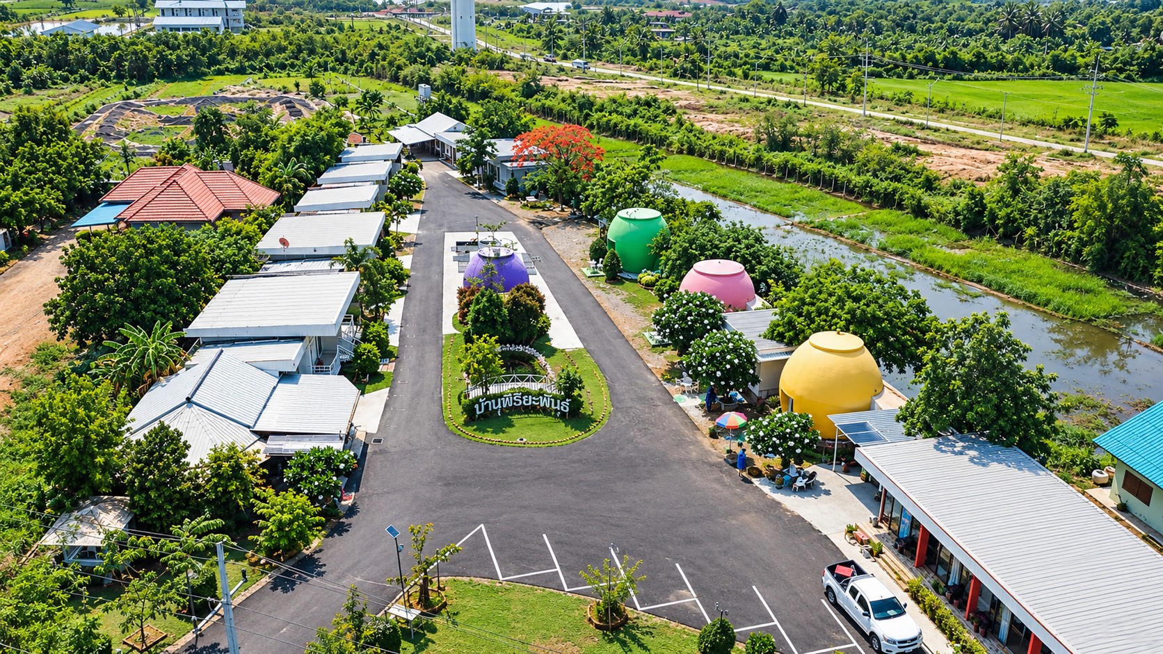 ภาพถ่ายมุมสูงของรีสอร์ท เห็นถนนทางเข้า บ้านโอ่งหลากสี และทุ่งนารอบด้าน